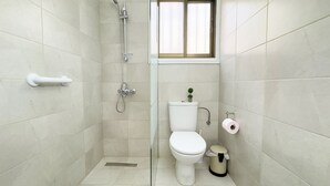 Un baño con inodoro, ducha, una ventana pequeña y un cubo de basura.