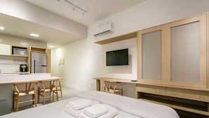 A modern hotel room with a bed, a desk, a chair, a TV, and a kitchenette. - Gastronomy | Swimming pool | Beachfront #CAJU04 (Florianópolis)
