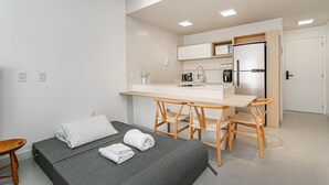A modern, compact room with a bed, a small table, and a kitchenette. - Gastronomy | Swimming pool | Beachfront #CAJU04 (Florianópolis)