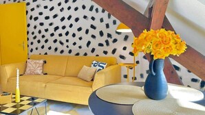 Un sof á amarillo, un jarrón azul con flores amarillas y una pared con estampado.