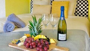 Una cama con un cojín a cuadros, una botella de vino y una bandeja de frutas.