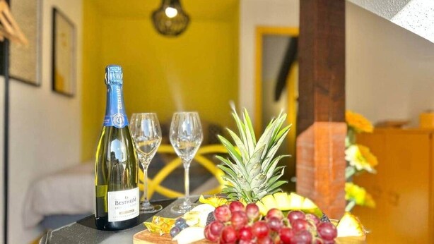 Una mesa con una botella de vino Bestheim, dos copas y una bandeja de frutas que incluye uvas y piña.