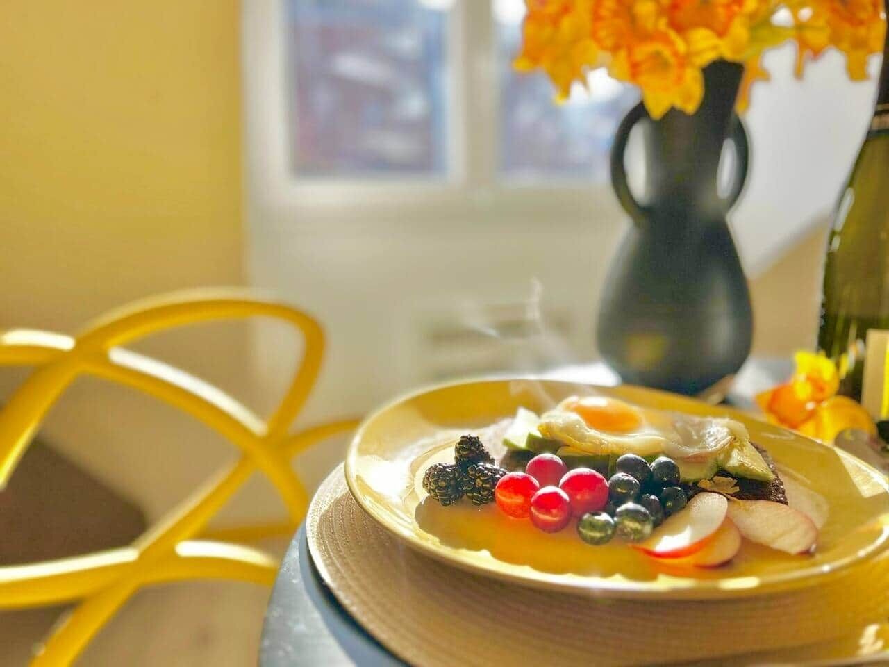 A breakfast plate with eggs, berries, and a slice of bread on a yellow table.