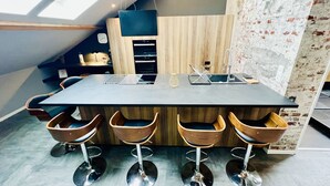 A modern kitchen with a large island, wooden bar stools, and a skylight. - Spacious, modern, quiet - Hypercentre Gérardmer (Gérardmer)