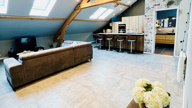 A spacious loft with a high ceiling, exposed wooden beams, a large sofa, a kitchen area, and a dining bar. - Spacious, modern, quiet - Hypercentre Gérardmer (Gérardmer)