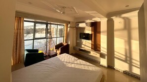A hotel room with a bed, a desk, a chair, a TV, and a window with curtains. - Soni's Mansion Shivsagar (Khajuraho)