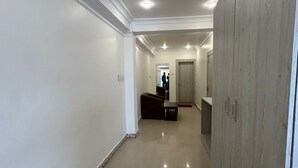 A hallway with a tiled floor, white walls, and a wooden wardrobe on the right. - Soni's Mansion Shivsagar (Khajuraho)