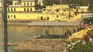 A riverside view with a temple in the background, a bridge, and a row of yellow buildings. - Soni's Mansion Shivsagar (Khajuraho)