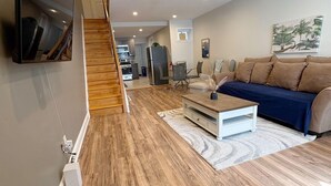 A modern living room with a wooden floor, a sofa, a TV mounted on the wall, and a staircase leading to another room. - Amazing 2BdRoom Townhome & Free Street Prkng in the University Section of Philly (Philadelphia)