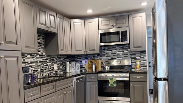 A modern kitchen with grey cabinets, stainless steel appliances, and a black marble backsplash. - Amazing 2BdRoom Townhome & Free Street Prkng in the University Section of Philly (Philadelphia)