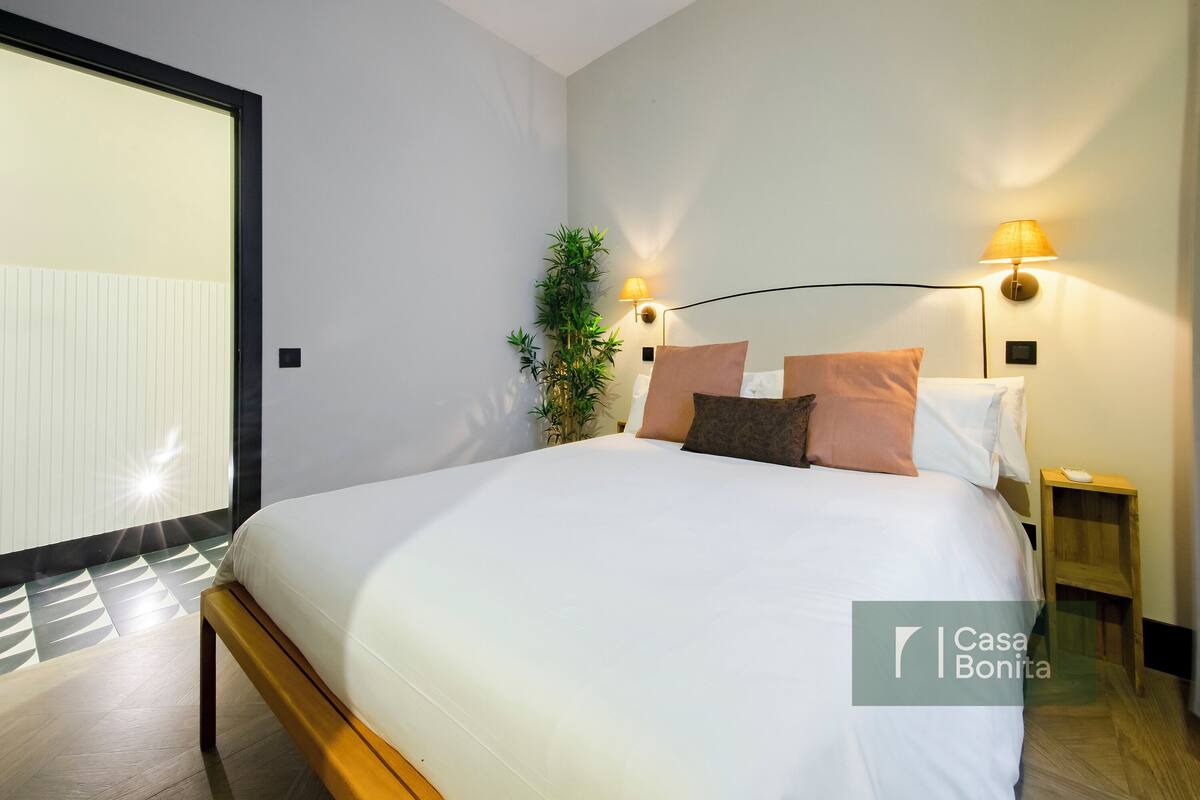 Un dormitorio moderno con una cama grande, dos lámparas de noche, una mesita auxiliar y una planta en maceta.