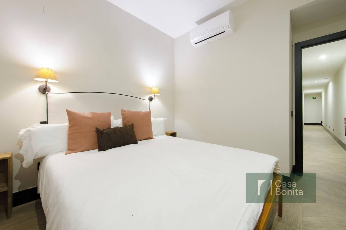 Habitación de hotel con una cama grande, dos lámparas de noche, una mesita de noche y un equipo de aire acondicionado.