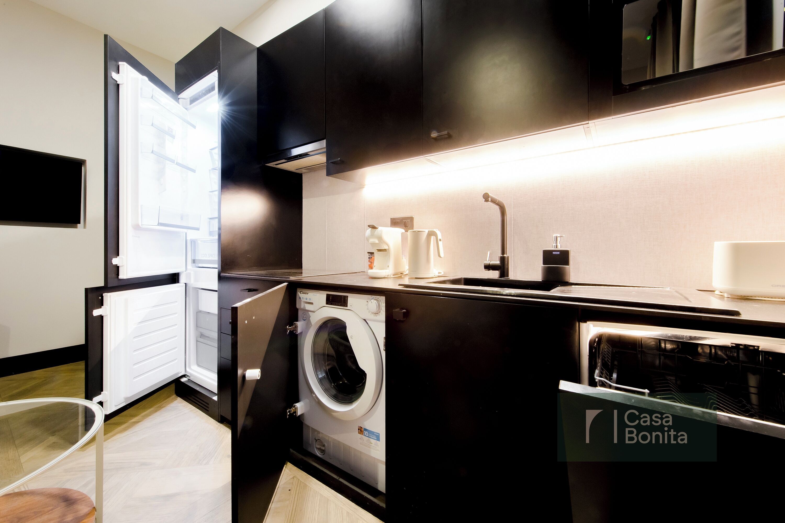 Une cuisine compacte équipée d’un lave-linge et d’un sèche-linge intégrés, d’un évier et d’un four à micro-ondes.