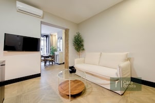 Ein Wohnzimmer mit einer Couch, einem Glastisch, einem Flachbildfernseher und einem Blumentopf.