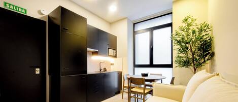 A compact kitchen with black cabinets, a dining area with a round table and chairs, a white sofa, and a large window with a view.