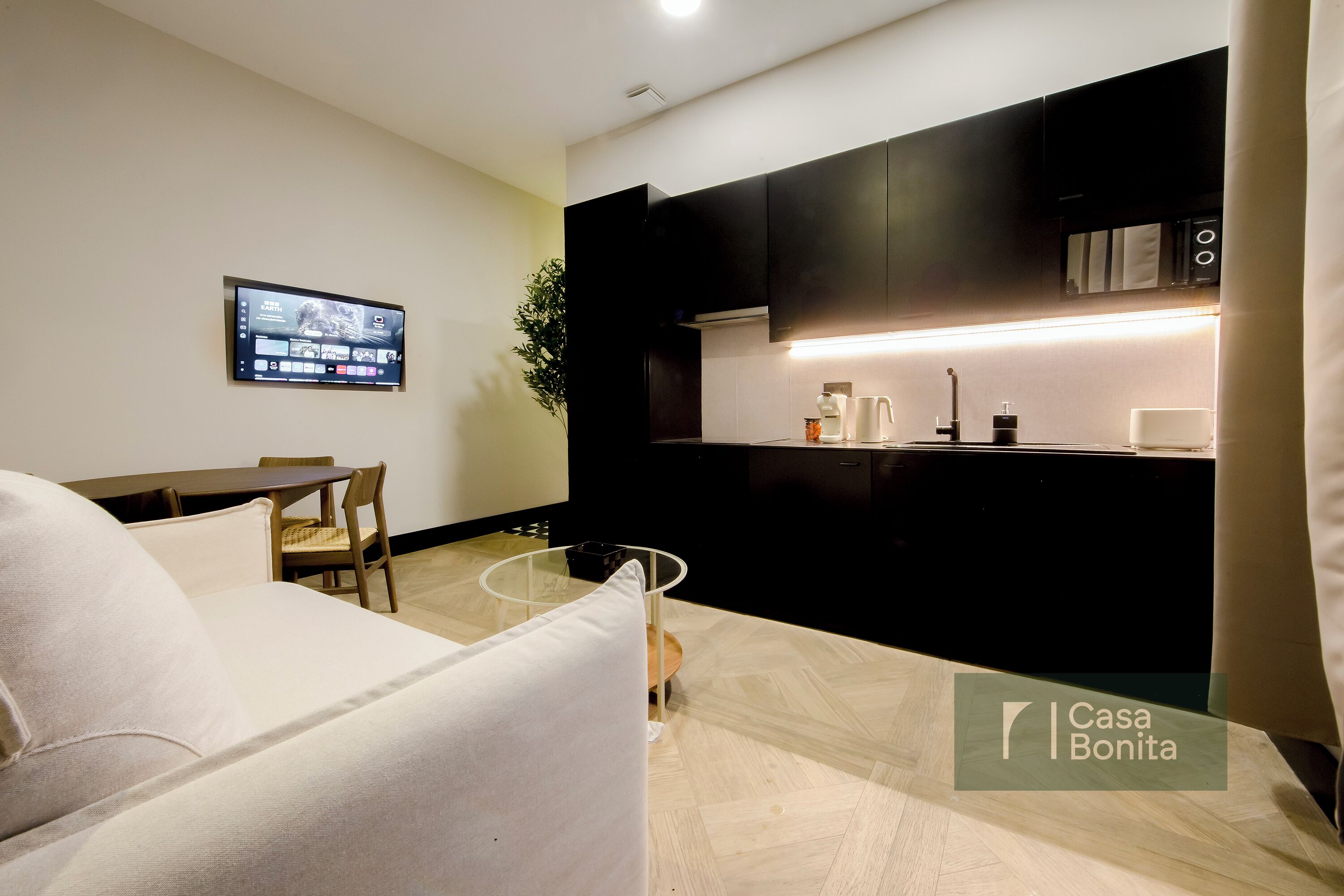 A modern living room with a sofa, a dining table, and a TV mounted on the wall.