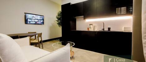 A modern living room with a sofa, a dining table, and a TV mounted on the wall.