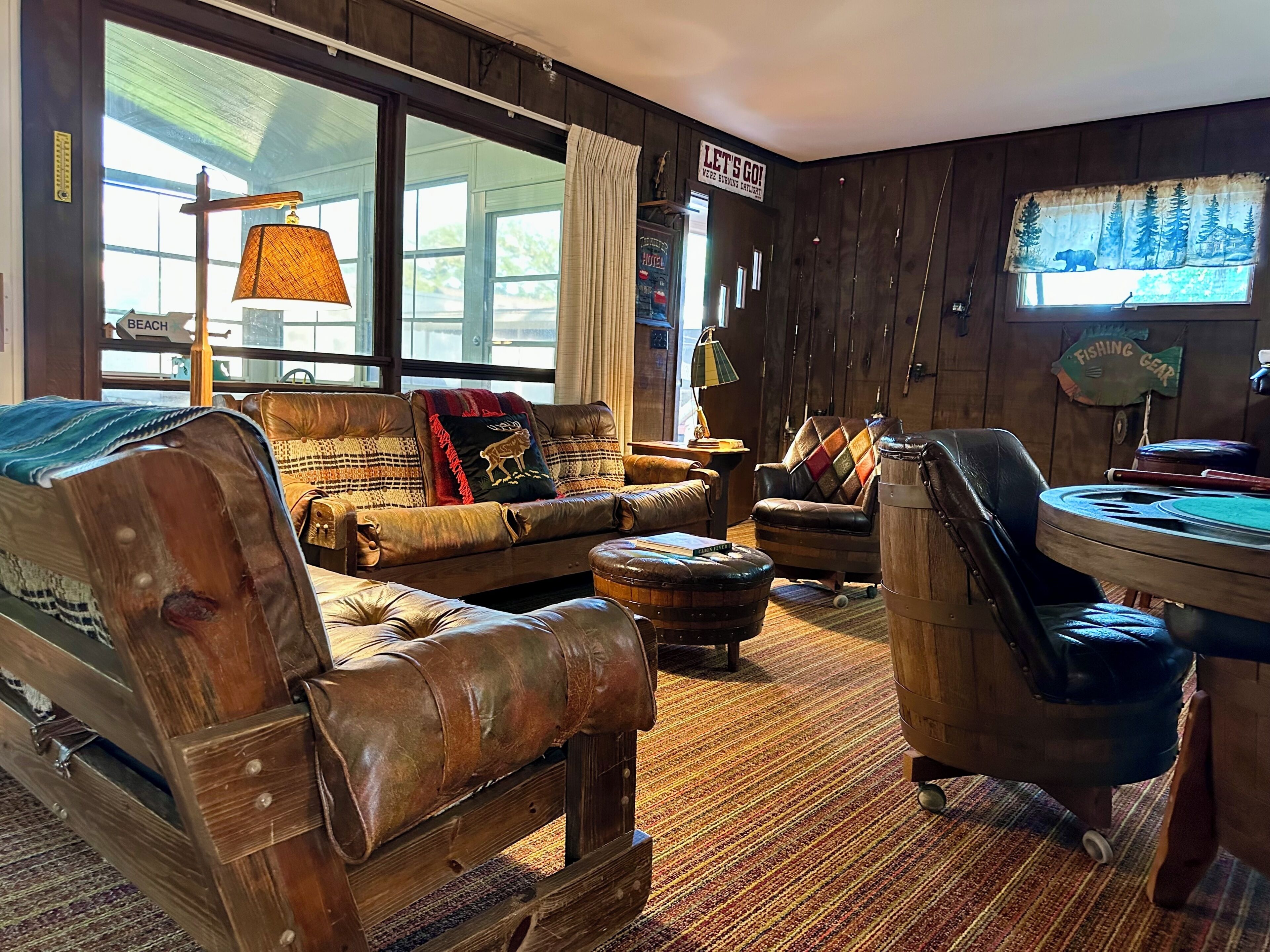 A cozy room with a leather sofa, a wooden chair, a small round table, and a window with a view of the outdoors.