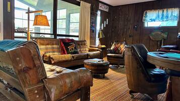 A cozy room with a leather sofa, a wooden chair, a small round table, and a window with a view of the outdoors.