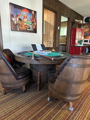 Une table de billard avec des queues de billard, un menu et un buffet rouge dans une pièce aux murs en bois et au tapis rayé.