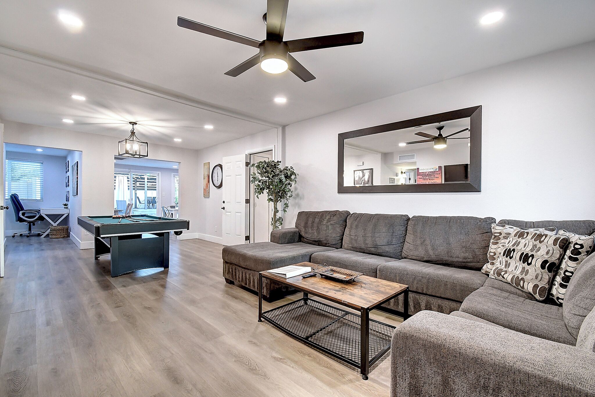 A modern living room with a pool table, a sofa, and a ceiling fan.