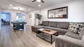 Een moderne woonkamer met een pooltafel, een bank en een plafondventilator.