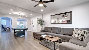 A modern living room with a pool table, a sofa, and a ceiling fan.