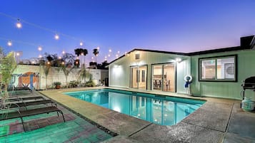 A swimming pool with lounge chairs, a covered patio, and string lights.