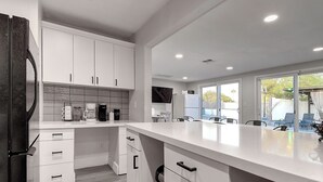 Een moderne keuken met witte kasten, een groot eiland en uitzicht op de omgeving.