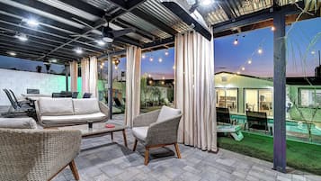 An outdoor patio area with wicker furniture, a pool, and string lights.
