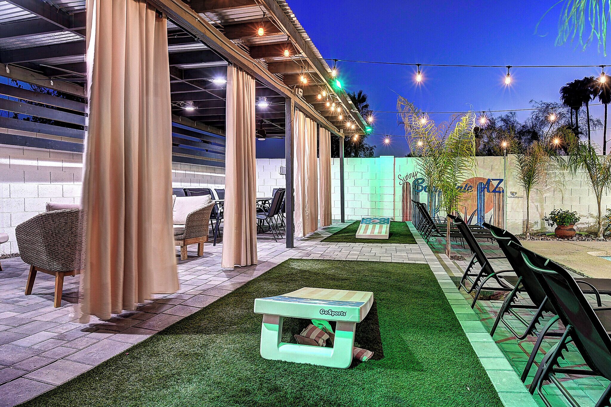 An outdoor patio area with a covered seating area, a GoSports table, and a brick wall with a sign.