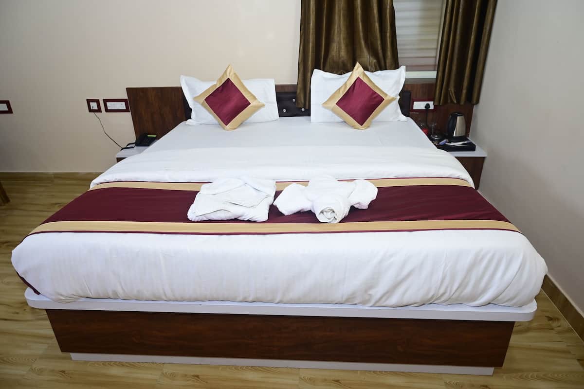 A neatly made bed with white and maroon bedding, two decorative pillows, and a pair of towels on the bed.
