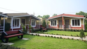 A row of two-story buildings with balconies, a paved pathway, and a small lawn area with benches. - THE SPARROW NEST ECO COTTAGE (Gop)