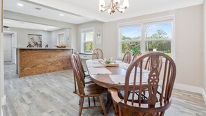 Un vaste espace dédié à la salle à manger, avec une table et des chaises en bois, un coin cuisine doté d’un plan de travail en bois, et de grandes fenêtres offrant une vue sur l’extérieur.