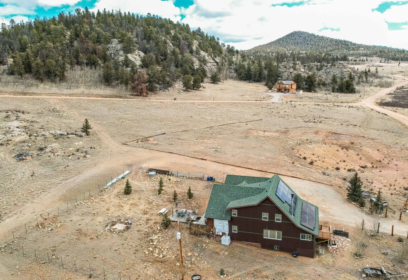 Una casa de fusta de planta única amb teulada verda, en un paisatge sec i obert amb vegetació escassa i una serralada de muntanyes al capvespre.