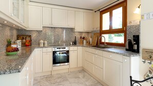 Eine moderne Küche mit weißen Schränken, Granit Arbeitsplatten, einem eingebauten Ofen und einem Fenster, das für natürliches Licht sorgt.