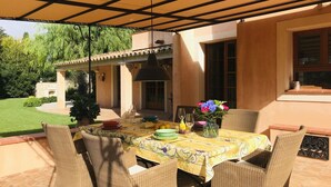 Eine Terrasse im Freien mit Esstisch, umgeben von Korbstühlen und einer Pergola darüber.