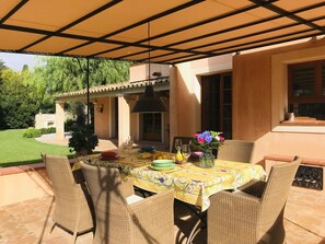 Eine Terrasse im Freien mit Esstisch, umgeben von Korbstühlen und einer Pergola darüber.