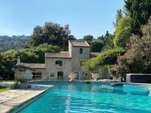 A pool area with a stone building in the background, surrounded by lush greenery. - Magnifique Maison historique (Saint Paul de Vence)
