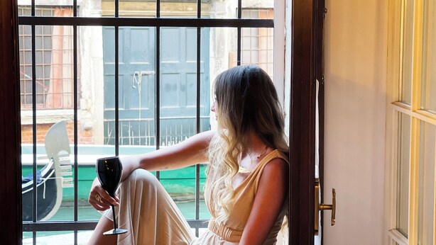 Une personne est assise près d’une fenêtre, d’où l’on peut voir un bâtiment et un espace vert à l’extérieur.