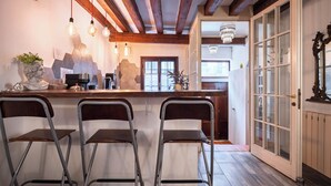 Un coin bar avec trois tabourets, une machine à café et un buste décoratif posé sur le comptoir.