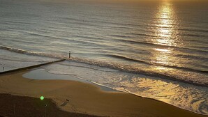 Een strand met een pier die in het water uitsteken, golven die zachtjes op het strand komen en de zon die ondergaat aan de horizon.