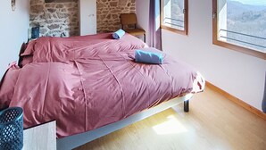 Ein Schlafzimmer mit Steinsandsteinwand, einem Bett mit rosafarbenem Überwurf, einem Fenster mit Bergblick und einer Holzbalkendecke.
