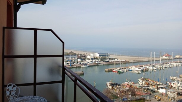 A balcony with a view of a marina, boats, and a distant shoreline. - CV020 – Cervia, penthouse with stunning sea view (Cervia)