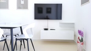 A modern room with a flat-screen TV mounted on the wall, a white dining table with chairs, and a white bench with a small table beside it. - CV020 – Cervia, penthouse with stunning sea view (Cervia)