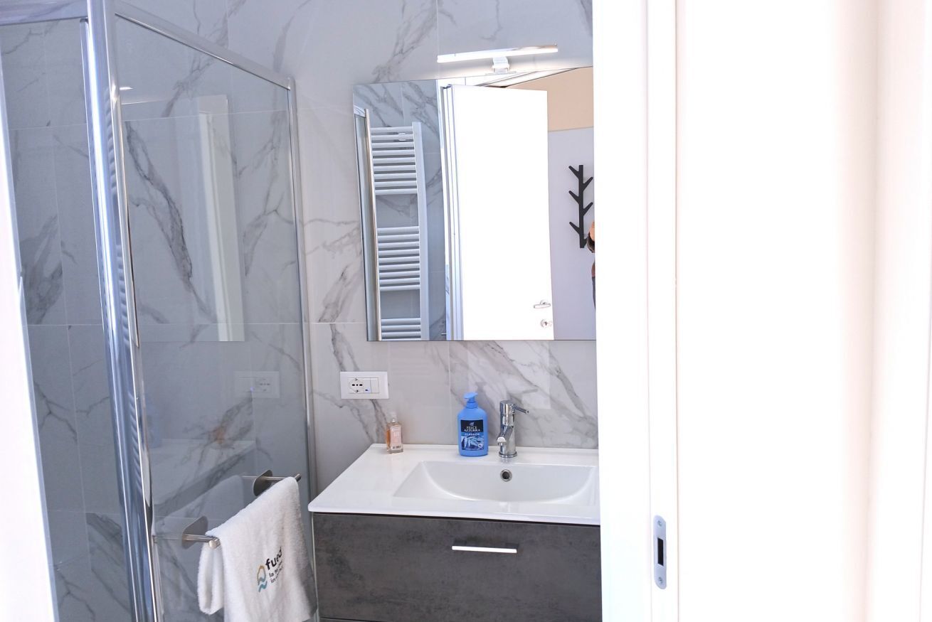 Een badkamer met een douchecabine van glas, een witte wastafel met een marmeren aanrechtblad en een spiegel boven de wastafel.