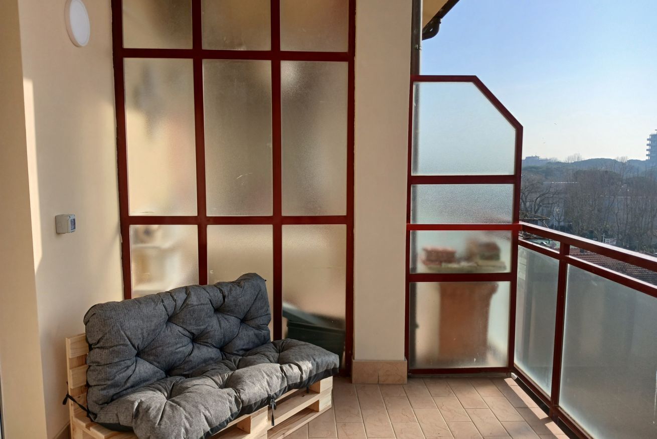 A balcony with a cushioned seating area, a view of the city, and a frosted glass partition.