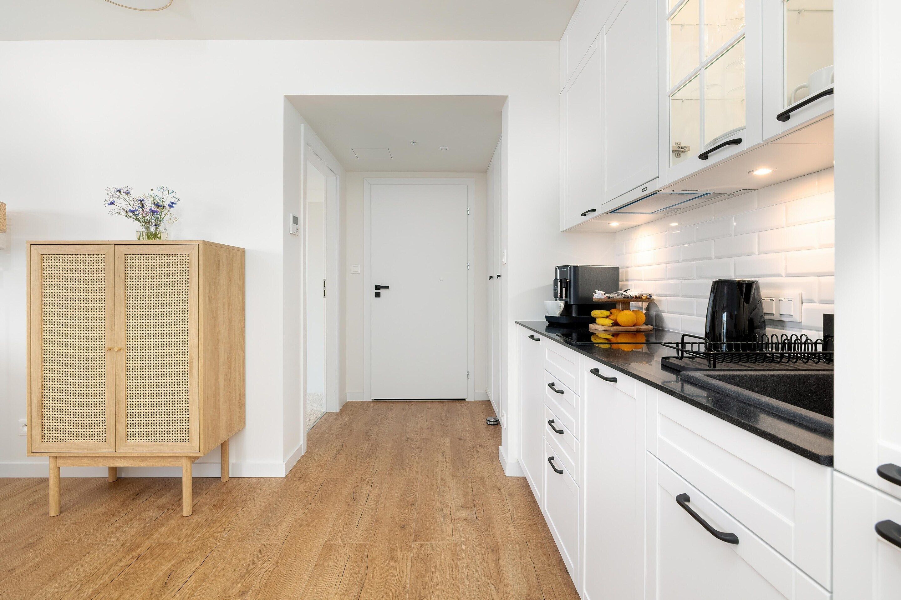 A modern kitchen with white cabinets, a wooden floor, and a black countertop.