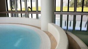 An indoor swimming pool with a curved edge, a white tiled floor, and a view of a green landscape through large windows. - Large Apartment With sea View, Indoor Pool (Rewal)