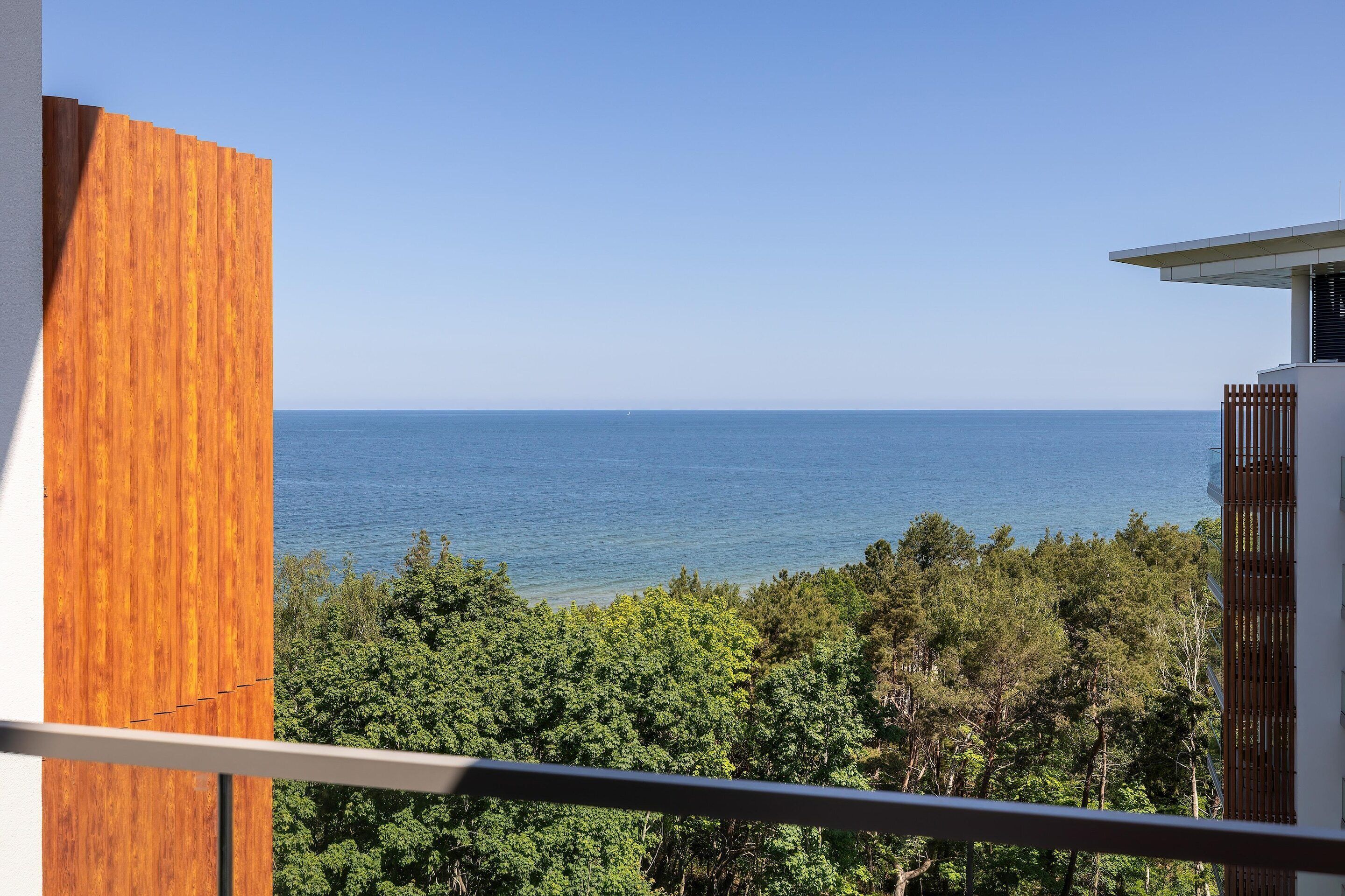 A balcony with a view of the sea and dense greenery.